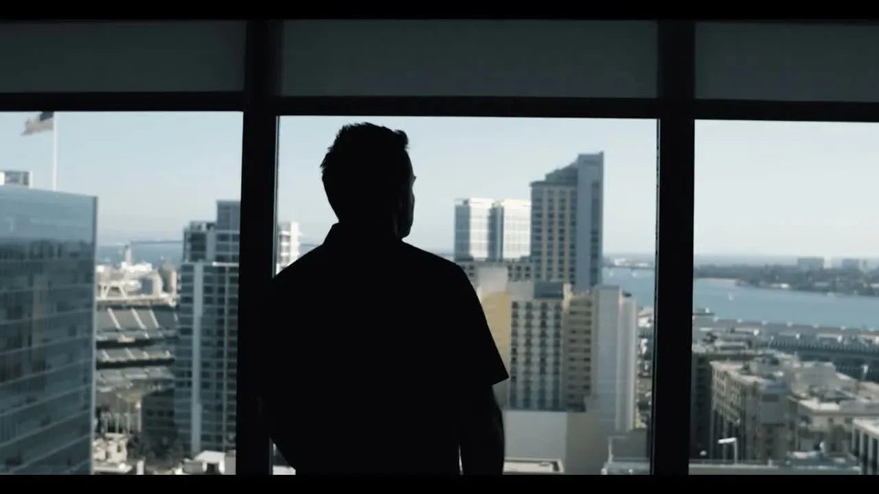 A founder standing alone at a high-rise window over a city skyline