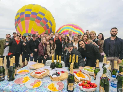 Members toasting at an outdoor brunch with hot air balloons behind them