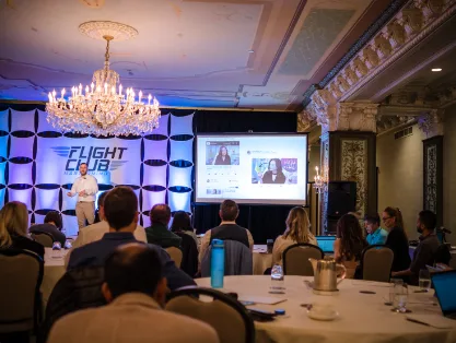 A presentation to members seated at round tables in a chandelier-lit ballroom