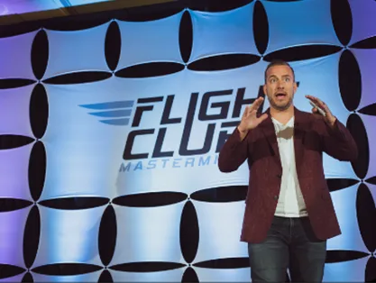 Glen Ledwell speaking on stage in front of the Flight Club backdrop