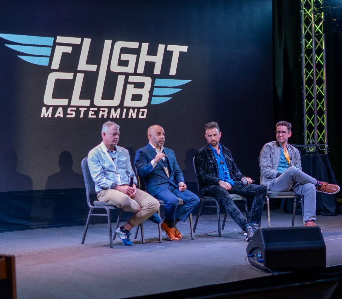 A panel of four members speaking on stage under the Flight Club Mastermind sign